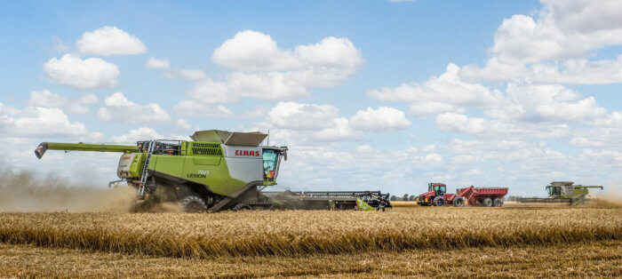 Australian agriculture scene with green wheat harvesting machinery and tractor with trailer in wheat field