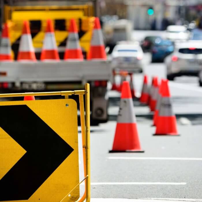 Traffic management signs and traffic cones in metropolitan city with cars on road.