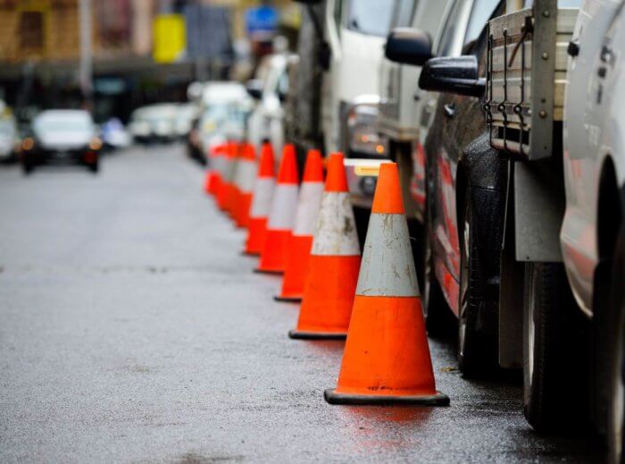 Traffic cones lined up next to cars on a wet metropolitan road.