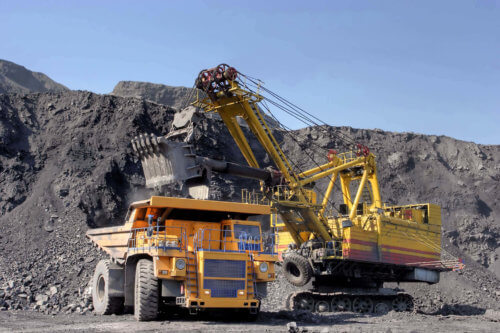 Excavator loading soil into yellow Komatsu dump truck at mine site.