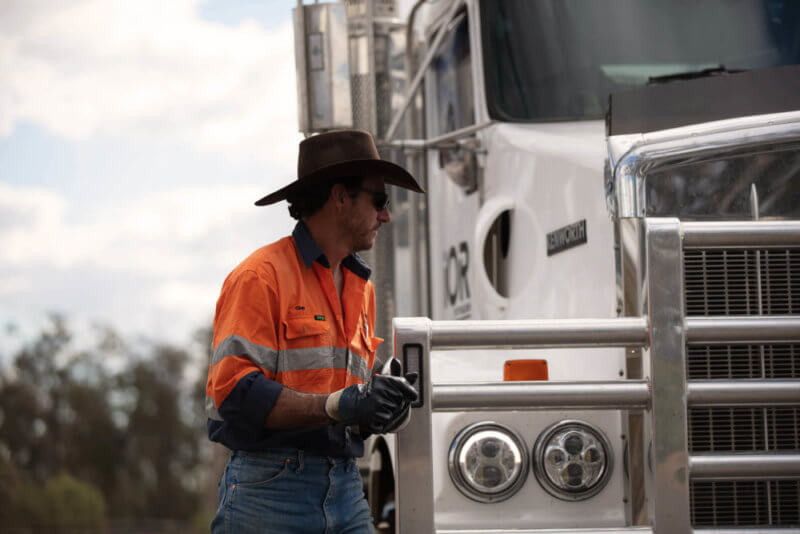 Truck driver wearing hat and gloves walking in front of IOR diesel truck