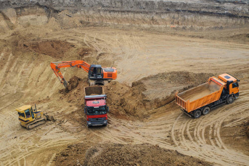 One red tip truck, one orange tip truck, bulldozer and excavator working together to excavate work site for construction