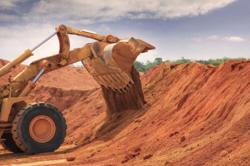 Backhoe loader unloading red soil at earthmoving site in remote Australia.
