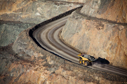 Yellow mining dump truck with full load driving along road in a mine located in rural Australia.